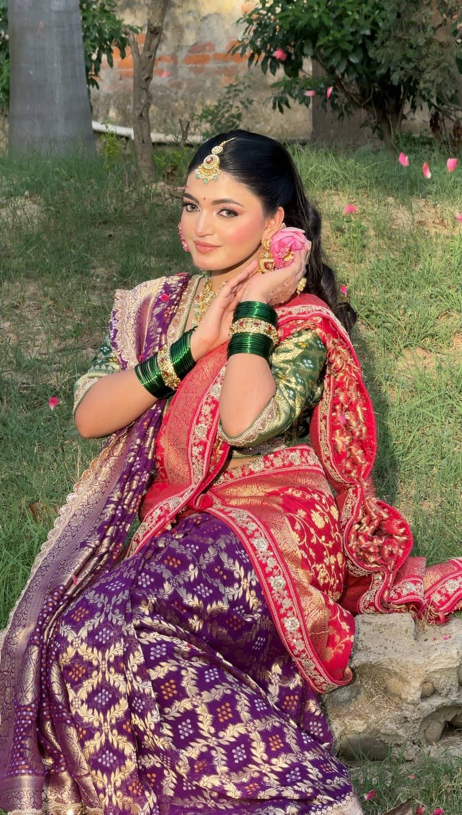 Bride seated outdoors in a purple and pink lehenga with green bangles